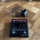 Černý efekt pedál s červeným pruhem a nápisy TC-HELICON harmony GXT a VOICETONE™. Zařízení obsahuje několik ovládacích knoflíků, přepínačů a displej…