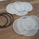 Sada bílých bubnových blan v různých velikostech a tři černé gumové prstence. Pět blan nese nápisy drum-tec a real feel, další čtyři mají nápis Mille…
