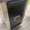 Černý transportní case s hliníkovými hranami a rohy. Na přední straně jsou umístěny dvě černé plastové ochranné lišty a uprostřed jedna kovová rukoje…