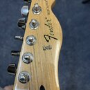 Fotografie zachycuje hlavu elektrické kytary z přírodního světlého dřeva s lakovaným povrchem. Na čele jsou umístěny nápisy "Fender" a "TELECASTER®".…