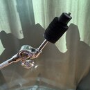 Detail chromovaného držáku na perkuse nebo činely s černou polstrovanou koncovkou. Na kovovém kloubu je viditelné logo Pearl. Povrch chromu je lesklý…