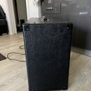 Fotografie zachycuje zadní stranu černého kytarového komba s povrchem z texturovaného vinylu. Rohy jsou chráněny kovovými kapslemi a v horní části je…