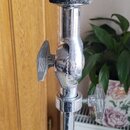 Detail horní části chromovaného stojanu s nastavitelně šroubovaným držákem. Na vrchu je umístěn tmavý, texturovaný gumový nebo pěnový kroužek. Povrch…
