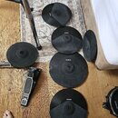 Sada černých gumových padů pro elektronické činely a jeden pedál. Na pěti padů je viditelné logo ALESIS, u jednoho z nich je nápis nečitelný. Pedál j…