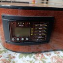 Detail na ovládací panel elektroniky zabudované v těle akustické kytary. Panel obsahuje displej, tlačítka a posuvníky s nápisy Bass, Midd., Treb., Pr…