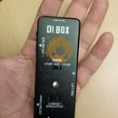 Černý kompaktní DI box s nápisem DI BOX. Na horní části je oranžový kruh s nápisy GAIN, -20dB, 0dB a +20dB. Přístroj obsahuje přepínače s popisky BAL…