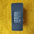 Černý obdélníkový adaptér s nálepkou na spodní straně. Na nálepce je text „Power: DC 9V Adapter Polarity: (+)—(o)—(-)“, nápis „Made in China“ a loga…