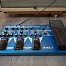 Modrý kytarový procesor Boss ME-50 Guitar Multiple Effects s černým expresním pedálem. Na přístroji jsou viditelné nápisy COSM a označení spínačů OD/…