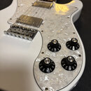 Bílá elektrická kytara s perleťovým pickguardem. Na knoflíkách jsou viditelné nápisy VOL. a TONE s číslováním 1 až 10. Nástroj má dva humbuckery a ch…
