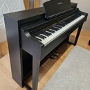 Černý digitální piano s klaviatura a integrovaným stojanem. Na notovém pultu je bílý nápis YAMAHA. Povrch nástroje vykazuje v horní části drobné oděr…