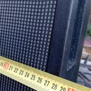 Detailní záběr na roh černého reproduktorového boxu s texturovaným povrchem a tmavě šedou ochrannou tkaninou. Přes hranu je přiložen žlutý skladací m…