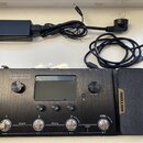 Černý kytarový procesor s nápisy AMPERO a Amp Modeler / Effects Processor. Na pravé straně je připevněn pedál s nápisem HOTONE. Zařízení obsahuje dis…