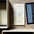 Fotografie zobrazuje papírový certifikát s nápisem Certificate a Warranty Card v černé barvě. Na certifikátu je uveden model NOD-1 a text „本产品检验合格 Th…