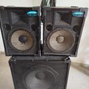 Tři černé reproduktory v odolných přepravních kufrech. Dva horní menší reproduktory mají v pravém horním rohu modré oválné štítky s nápisem mek PA 11…