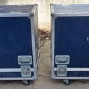Dvě modré transportní bedny na kolečkách s kovovými hranami a úchyty. Na přední straně každé bedny je bílý nápis UPA-2P. Povrch beden vykazuje známky…
