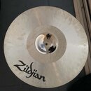 Kruhový činel z kovového materiálu s viditelným povrchovým opracováním. Na povrchu je černý nápis Zildjian. V centru se nachází otvor a bílá nálepka…