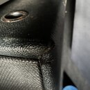 Detailní záběr na roh černého reproduktoru nebo zesilovače. Povrch je kombinací texturovaného černého vinylu a látkového potahu. V horní části jsou v…
