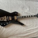 Černá elektrická kytara s atypickým, ostře hranatým tvarem těla. Na hlavě hmatníku je bílé logo Washburn. Nástroj má dva humbuckery, stříbrný hardwar…