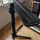 Černý kovový stojan na klávesové nástroje s dlouhou horní deskou. Stojan má skládací konstrukci a na koncích desky jsou integrované úchopy. Povrch je…
