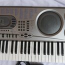 Stříbrný digitální klavír značky CASIO s nápisem MUSICAL INFORMATION SYSTEM. Nástroj má bílé a černé klávesy, vestavěné reproduktory a ovládací panel…