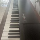 Černý digitální klavír s bílými a černými klávesami. Na ovládacím panelu je nápis YAMAHA ELECTRONIC PIANO p15 a červená kontrolka s nápisem POWER u v…