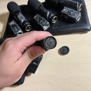 Ruka drží černý mikrofon s odšroubovanou mřížkou, která leží vedle na stole. V pozadí je černý přepravní kufr s nápisem audio-technica, ve kterém jso…