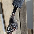 Kovový držák s nápisem TAMA HARDWARE a černým plastovým uchopovacím prvkem. Horní část je opatřena černou texturovanou vložkou a dvěma červenými plas…