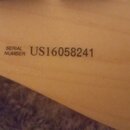 Detailní záběr na světlý dřevěný povrch hudebního nástroje. Na povrchu je černý nápis SERIAL NUMBER a vedle něj sériové číslo US16058241. Povrch je h…