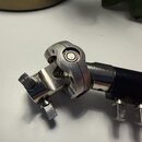 Detailní pohled na kovovou hlavu hudebního nástroje s černým hnedkem. Jsou vidět čtyři kovové ladičky a mechanismus s kuličkovým ložiskem. Povrch kov…