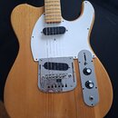 Elektrická kytara s přírodním dřevěným povrchem těla a světlým hnedým hmatníkem. Nástroj má bílý pickguard, chromovaný most s krytem a ovládací panel…