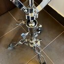 Detail spodní části chromovaného stativu s trojramennou základnou. Na kovových částech jsou vidět šroubovací knoflíky pro utahování a na koncích noho…