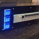 Černý kovový box s ovládacím panelem. Na přední straně jsou tři modré digitální displeje s hodnotami 244V/00.0A (L1), 242V/00.0A (L2) a 245V/00.0A (L…