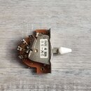 Elektrický přepínač s bílou plastovou pákou a kovovým tělem, upevněný na hnědém podkladu. Na bílém štítku je uveden nápis DM-50 MADE IN JAPAN. V levé…