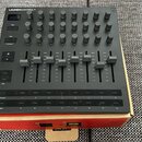 Černý MIDI kontrolér s nápisem LAUNCHCONTROL XL. Horní část obsahuje mřížku šesti řad s otočnými knoflíky, pod nimi je osm posuvníků a v dolní části…