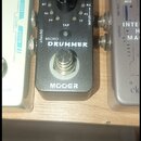 Černý efekt pedál s nápisy MICRO DRUMMER a MOOER. Na horní části je ovládací knoflík VOLUME, tlačítko TAP a několik malých LED indikátorů s označením…