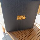 Černý textilní kryt na hudební zařízení, umístěný na dřevěném stole. Uprostřed je žluté logo s nápisem MARK WORLD a stylizovanou postavou. Povrch lát…
