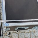 Černý transportní case s hliníkovými hranami a kovovými rohy. Na přední straně je umístěna černá plastová rukojeť a dvě kovové zavírací zámky. Přes h…