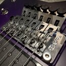 Detailní pohled na chromovaný kobylku typu Floyd Rose na fialovém trupu elektrické kytary. Na pravé straně je vyryt nápis FloydRose. Povrch kovu vyka…