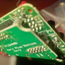 Fotografie zachycuje zelený plošný spoj s připájenými elektronickými součástkami a kovovými kontakty. Na desce je bílý nápis FISHMAN, Aero Plus Botto…