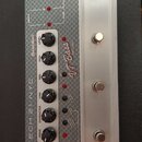 Stříbrný kytarový pedál s kovovým šasi a texturovaným horním panelem. Na přístroji jsou nápisy TECH 21 NYC, SANSAMP a VT Bass DELUXE. Obsahuje šest č…