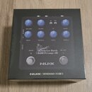Fotografie znázorňuje krabici s basovým předzesilovačem NUX. Na zařízení jsou vidět ovládací knoflíky s popisky VOLUME, BLEND, IR, DRIVE, BASS, MIDDL…