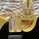 Žlutá kytara s černým pickguardem a dřevěný kráček. Na kráčku je nápis ALLPARTS LIC. BY FENDER a níže menší text LINDY FRALINO MODEL. Na dřevěném díl…