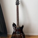 Elektrická kytara s tmavě hnědým průhledným lakem a vyznačenou dřevěnou strukturou. Na hlavě hmatníku je bílý nápis Ibanez. Nástroj má dva humbuckery…