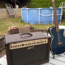 Kytarový kombozesilovač s hnědým texturovaným povrchem a černou ochrannou síťkou. Na předním panelu je nápis MEGA VOICE ACOUSTIC AMPLIFIER a v pravém…