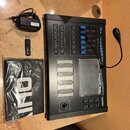 Černý MIDI kontrolér s modrými detaily a řadou posuvníků. Na zařízení jsou viditelné nápisy "MASTER CONTROLLER" a "QUIVER". Součástí je napájecí adap…