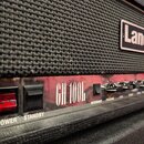 Detail kytarového komba s černou textilní maskou a logem Laney. Na ovládacím panelu je nápis GH 100L, červený vypínač s označením POWER a černý vypín…