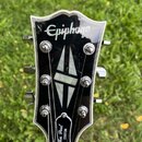 Černá hlava kytary s bílým lemováním a nápisem Epiphone. Uprostřed je vykládaný perleťový symbol ve tvaru kosočtverce a v dolní části nápis Les Paul…