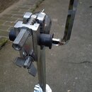 Detail kovového stojanu s chromovaným povrchem. Na fotce je vidět mechanismus s utahovacími šrouby a dvěma černými plastovými krytkami. Povrch kovu v…