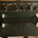 Černý kytarový kombo zesilovač s texturovaným povrchem a nápisy INPUT, GAIN, Overdrive, Clean, TREBLE, BASS, VOLUME, HEAD / LINE PHONE / OUT a POWER…
