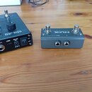 Na dřevěném stole leží dvě zařízení. Vlevo je černý efektový procesor s nápisem MG-30 VERSATILE MODELLER, který má několik ovládacích knoflíků a kone…